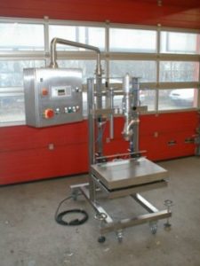 Metallische Abfüllwaage mit Display und Bedienelementen in industrieller Umgebung, vor rot gestrichenen Wänden und Fenstern. Kabel und Schalter sichtbar.