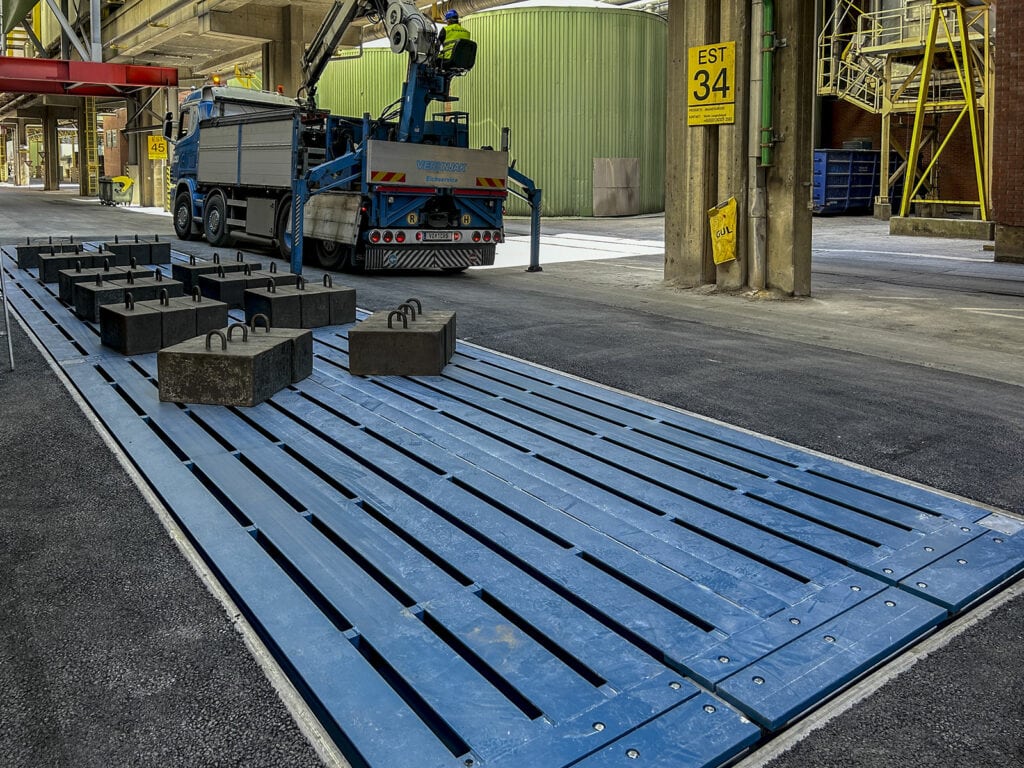 Industriegebiet mit Kran und Prüfgewichten auf Unterflurwaage zur Eichung