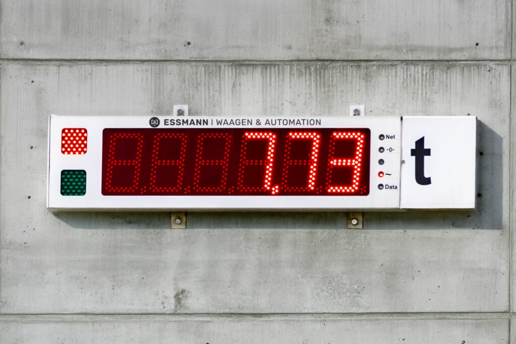 Weiße Fernanzeige mit roter Digitalanzeige mit 7,73 Tonnen, einer rot leuchtenden Ampel und der Aufschrift ESSMANN Waagen und Automation.