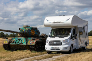 Wohnmobil neben bunt bemaltem Panzer auf Feld