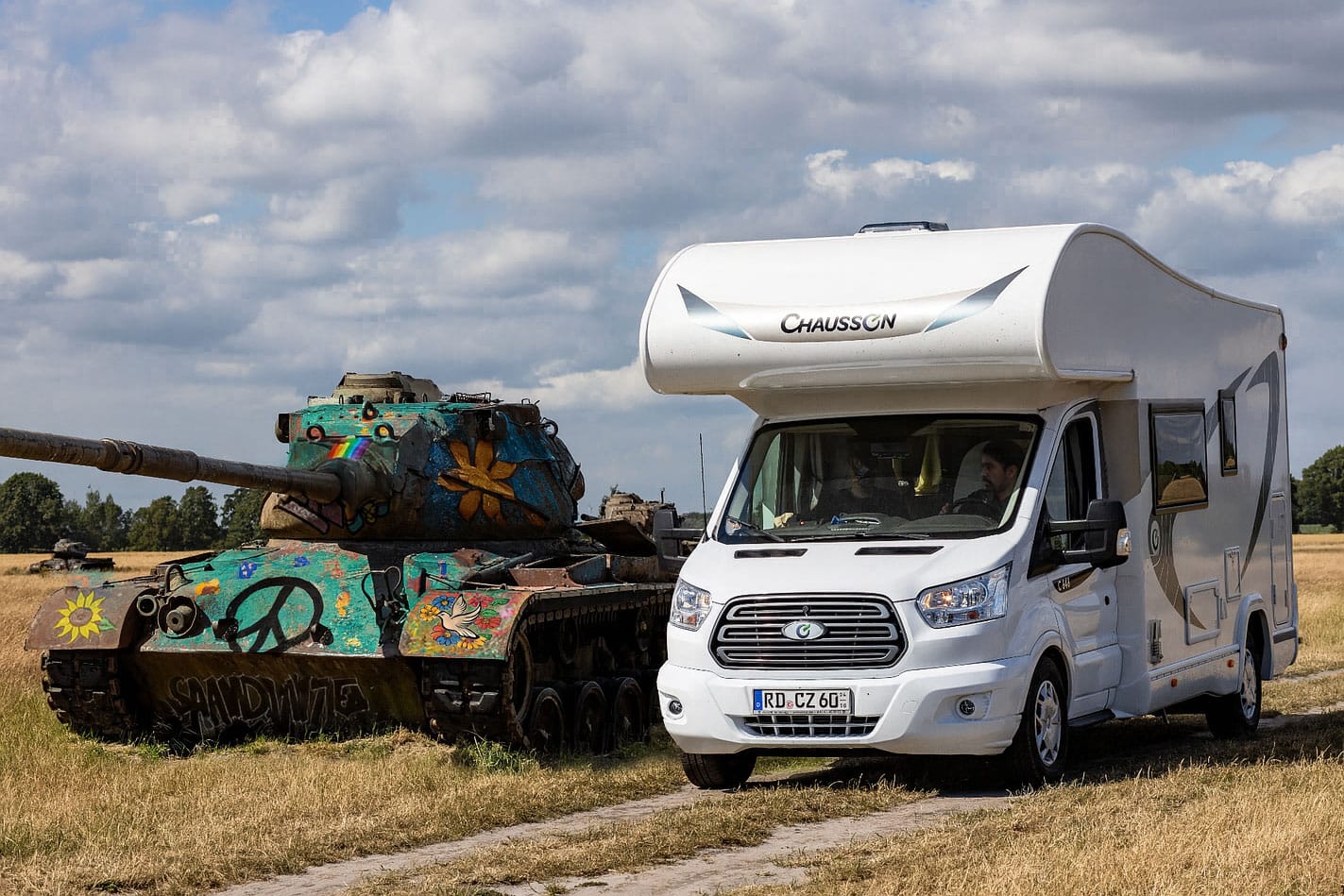 Wohnmobil neben bunt bemaltem Panzer auf Feld