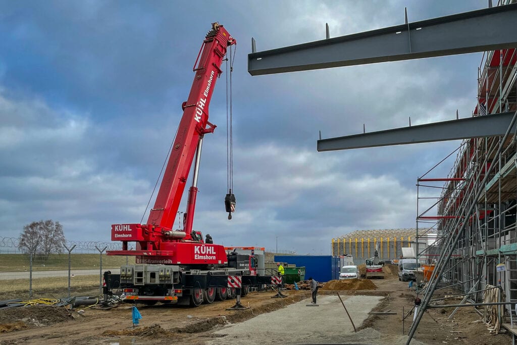 Ein roter Autokran bringt sich in Stellung, um das Betonfundament an seinen Standort zu heben
