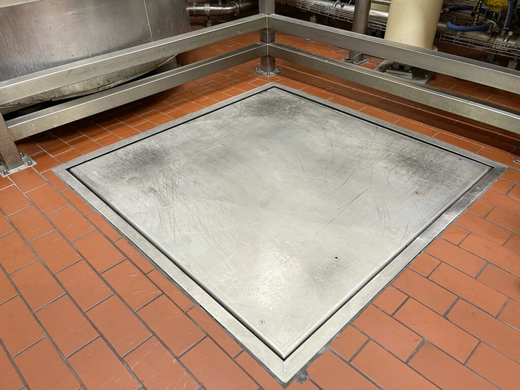 Bodenwaage aus Metall bündig im roten Fliesenboden, umgeben von Edelstahlgeländern und Industrieanlagen. Geeignet für industrielle Anwendungen, robust und funktional.