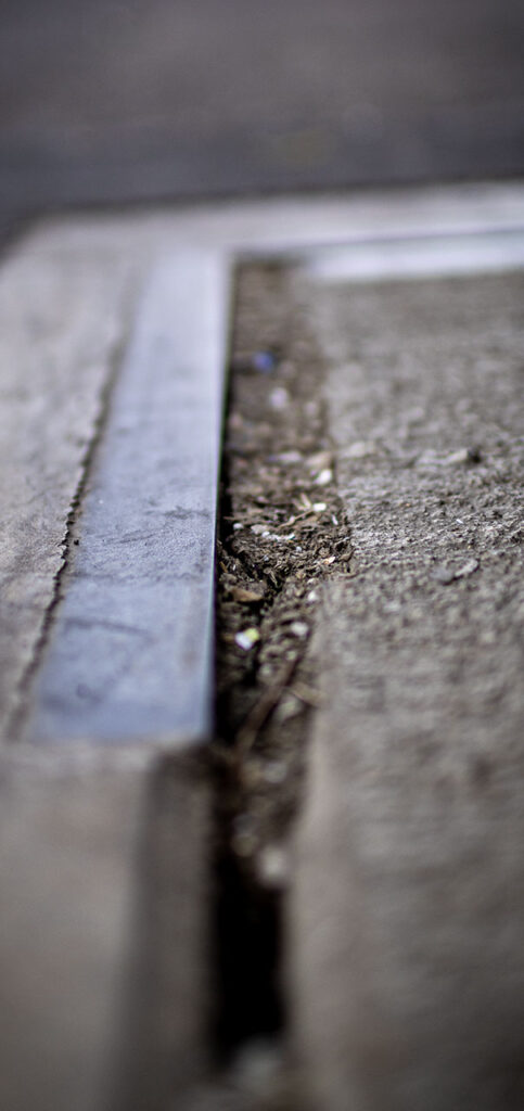 Nahaufnahme einer Fahrzeugwaage mit Metallkante und einer Fuge voller Schmutz. Fokus liegt auf der Textur, als Detail für Frühjahrs-Check von Fahrzeugwaagen im Steinbruch & Kieswerk.